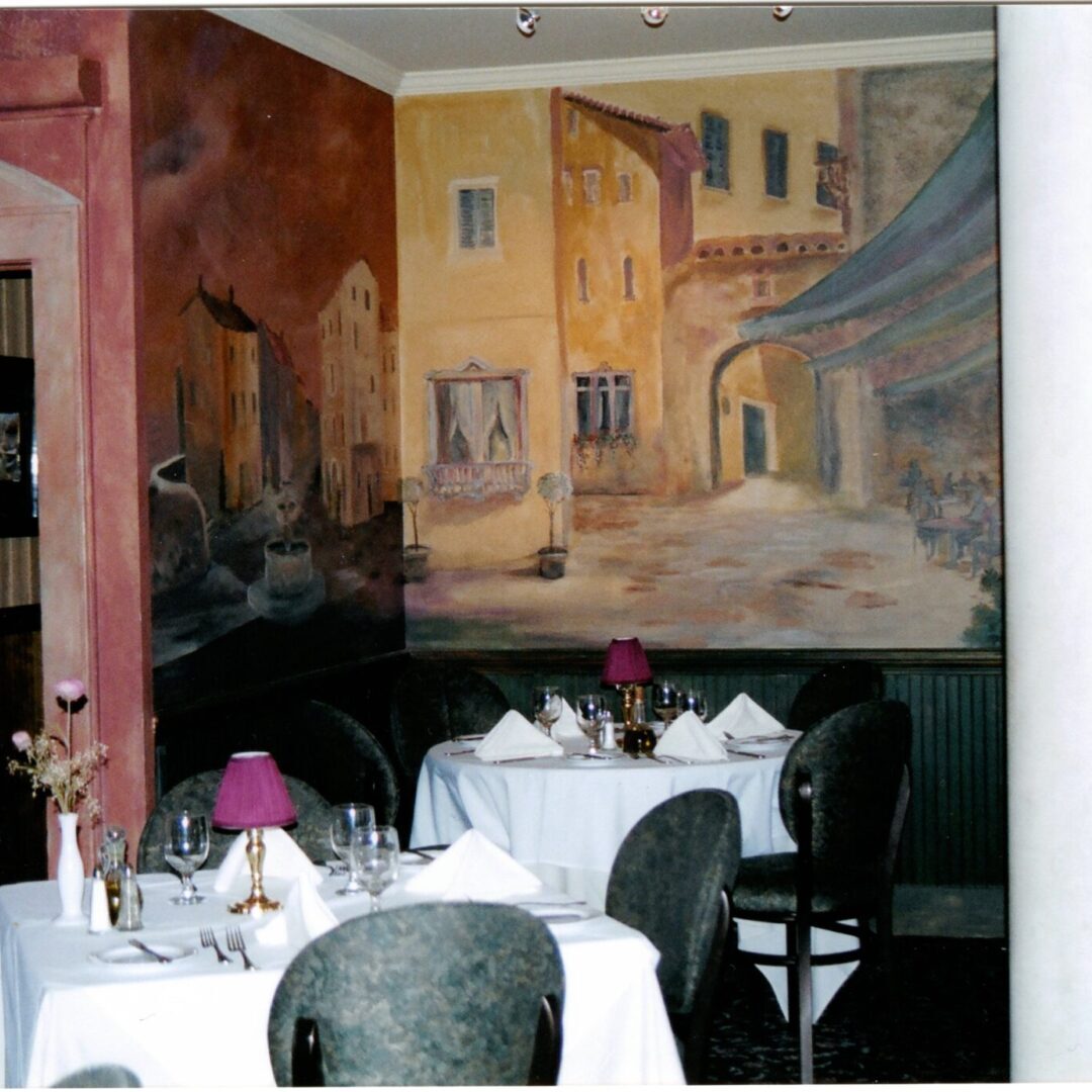 A restaurant with tables and chairs in front of a painting.